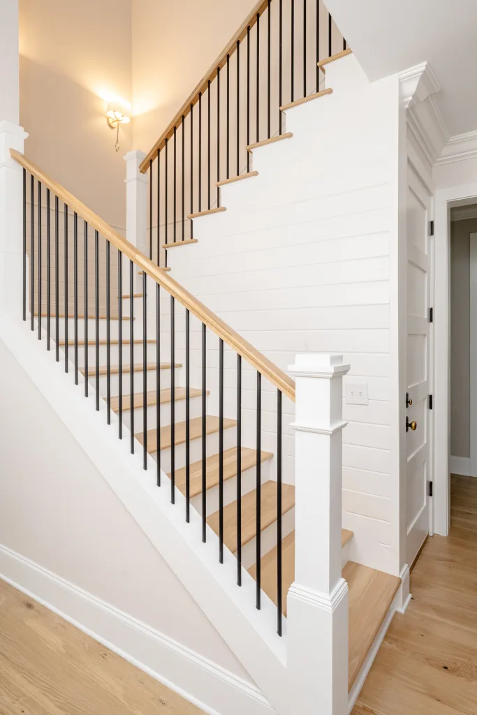 Staircase with wood treads, black iron balusters, and brass wall sconce in Charleston, SC